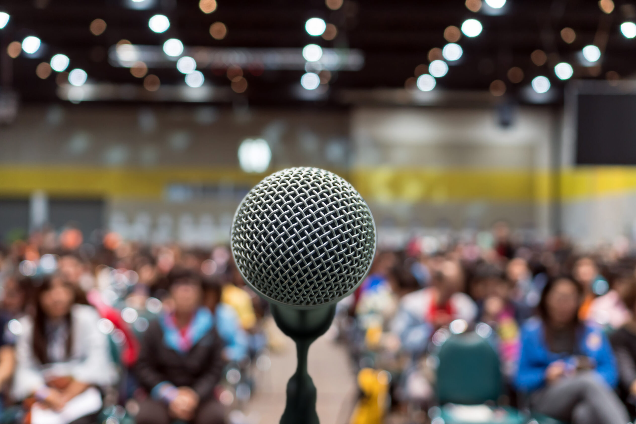 Microphone over the Abstract blurred photo of conference hall or seminar room in Exhibition Center background with Speakers on the stage and attendee background, Business meeting and education concept